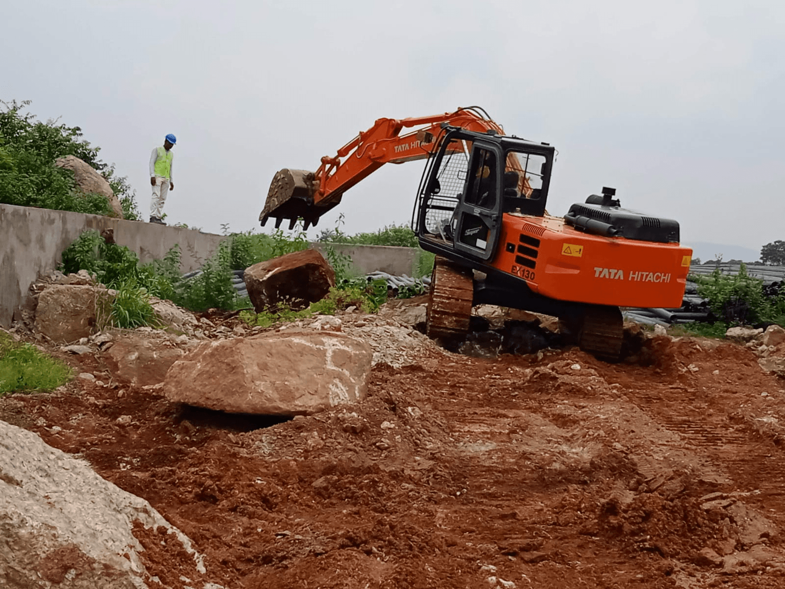 Excavator operating around large rock at an active site