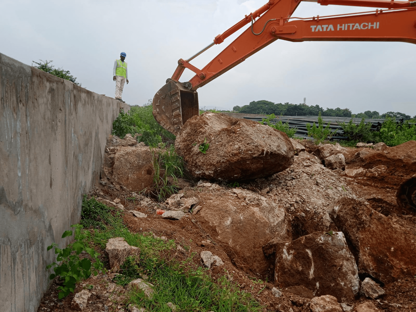 Excavator progressing rock removal beside a site boundary